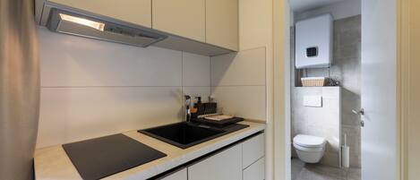 Una cocina moderna con una placa de inducción negra, una campana extractora de acero inoxidable y un salpicadero de azulejos blancos.