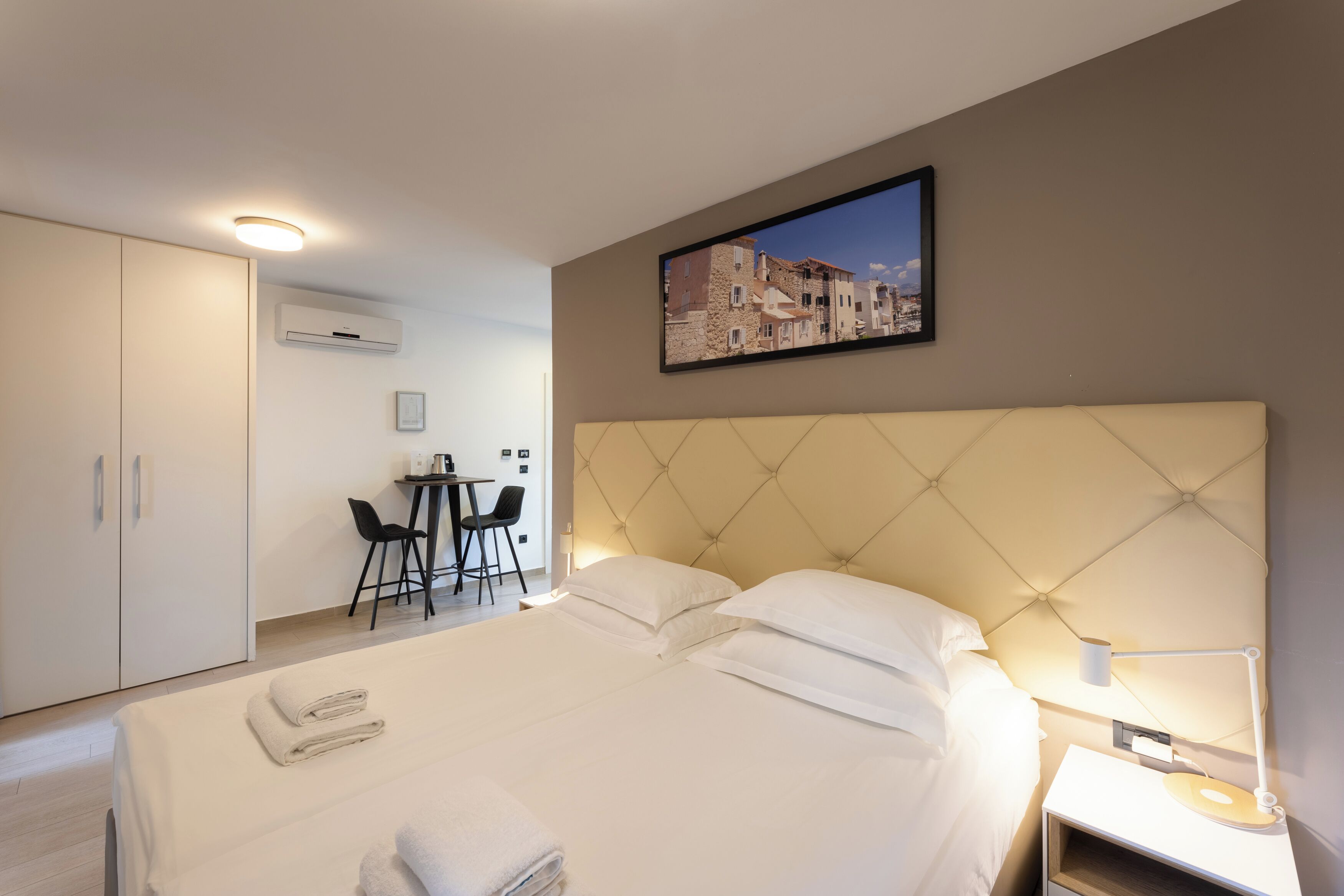 Habitación de hotel con una cama grande, un escritorio con dos sillas, un equipo de aire acondicionado y un cuadro en la pared.