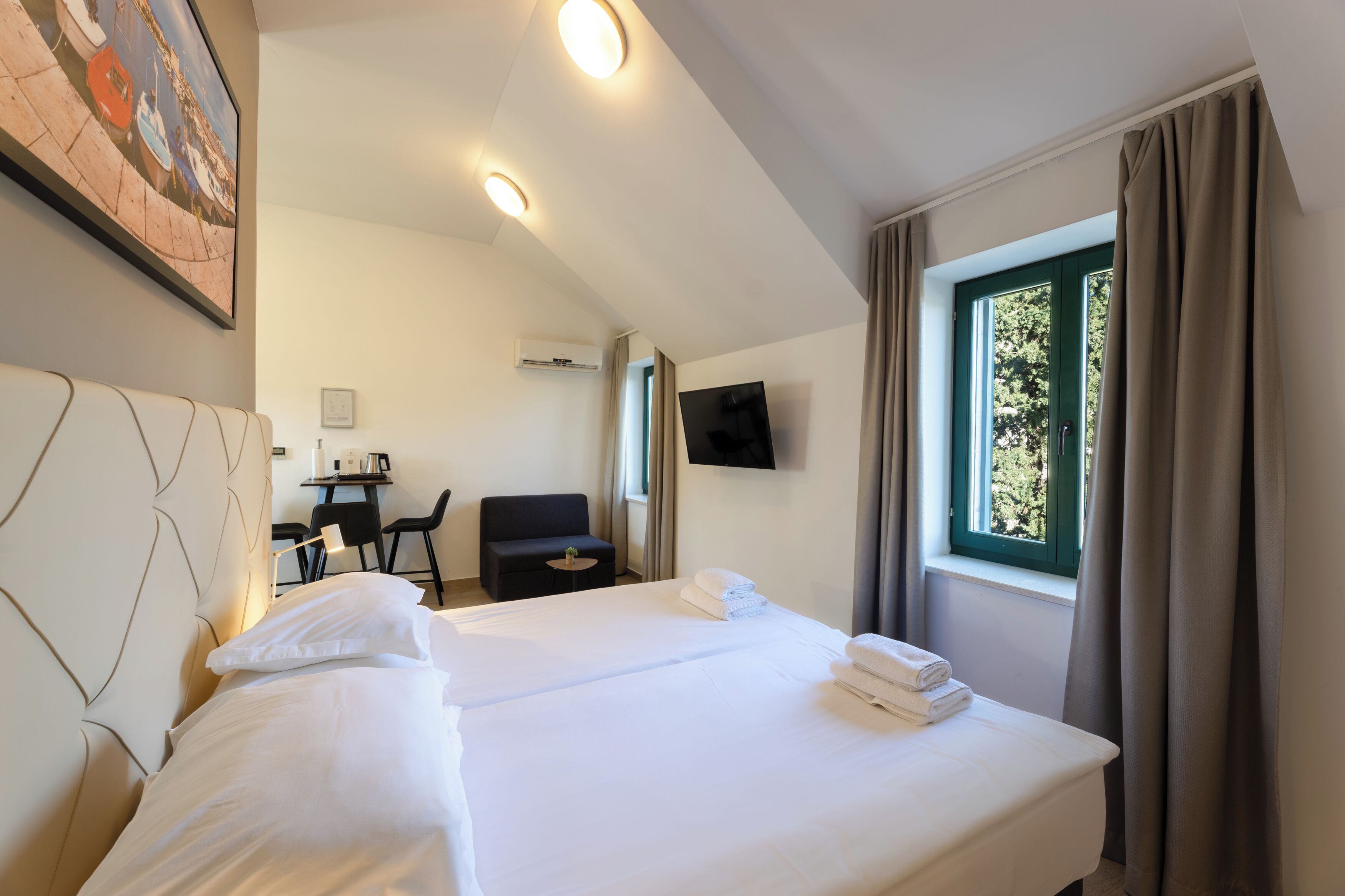 A hotel room with two beds, a desk, a chair, a TV, and a window with curtains.