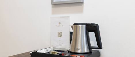 Una cafetera sobre una mesa de madera, con un certificado enmarcado y un código QR en la pared de fondo.