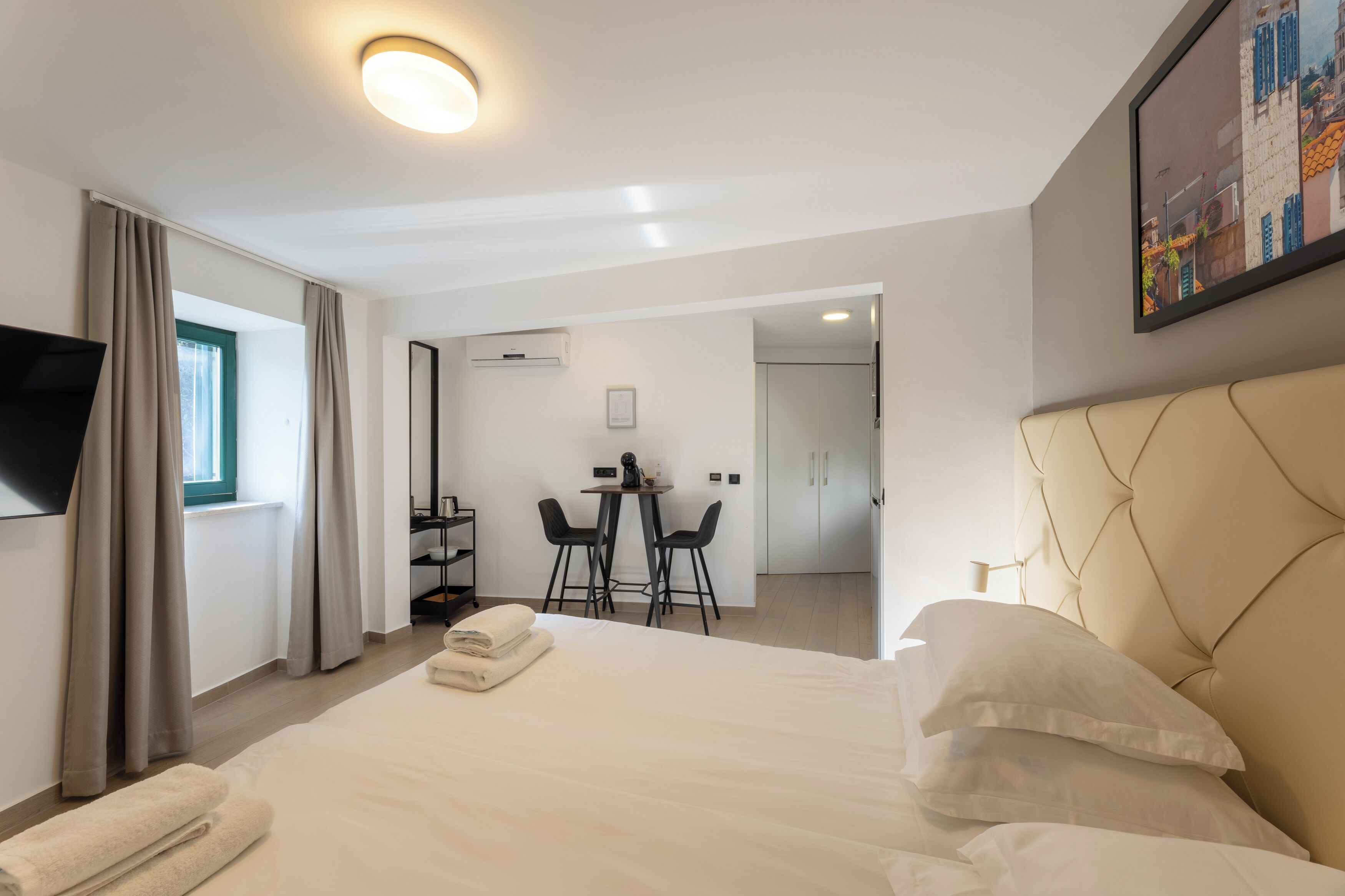 A hotel room with a bed, a desk with two chairs, a TV, and a painting on the wall.