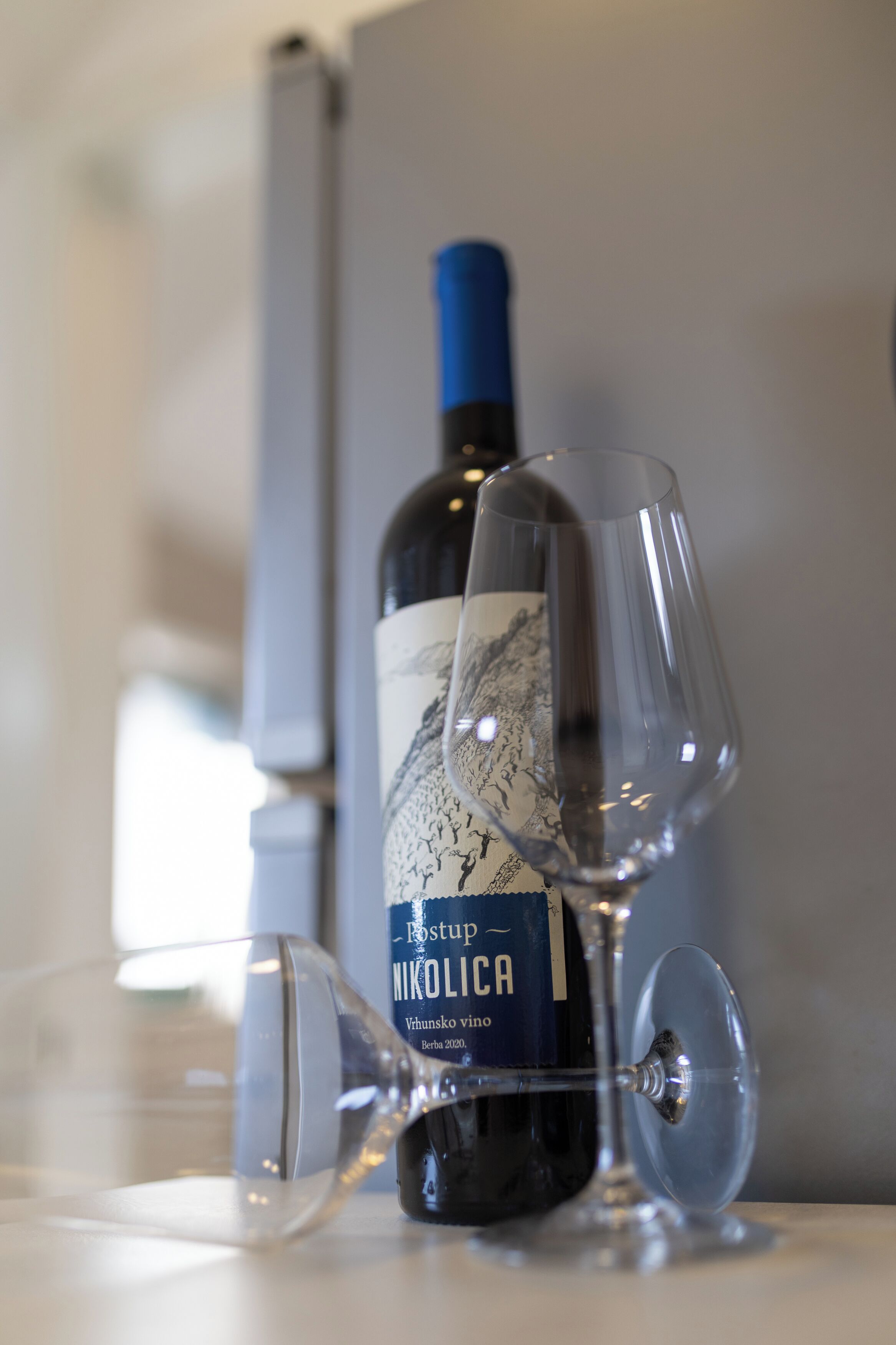 Una bottiglia di vino NIKO LICA e due bicchieri da vino su un tavolo.