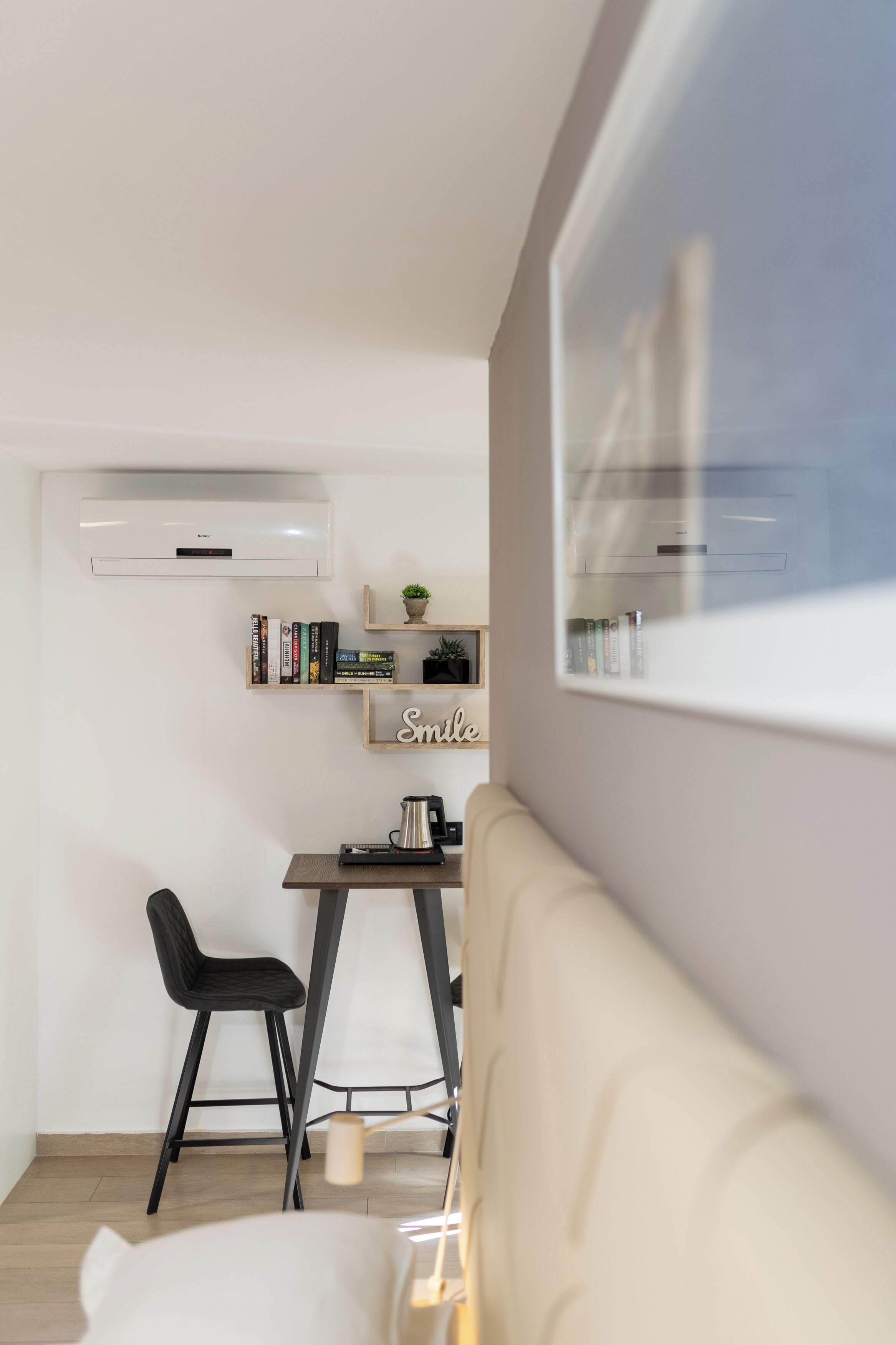 A modern, minimalist living space with a sofa, a small dining table with chairs, a bookshelf, and a wall-mounted air conditioner.