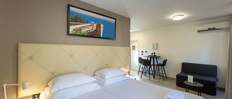 A hotel room with a large bed, a desk, a chair, a sofa, and a painting of a coastal scene.
