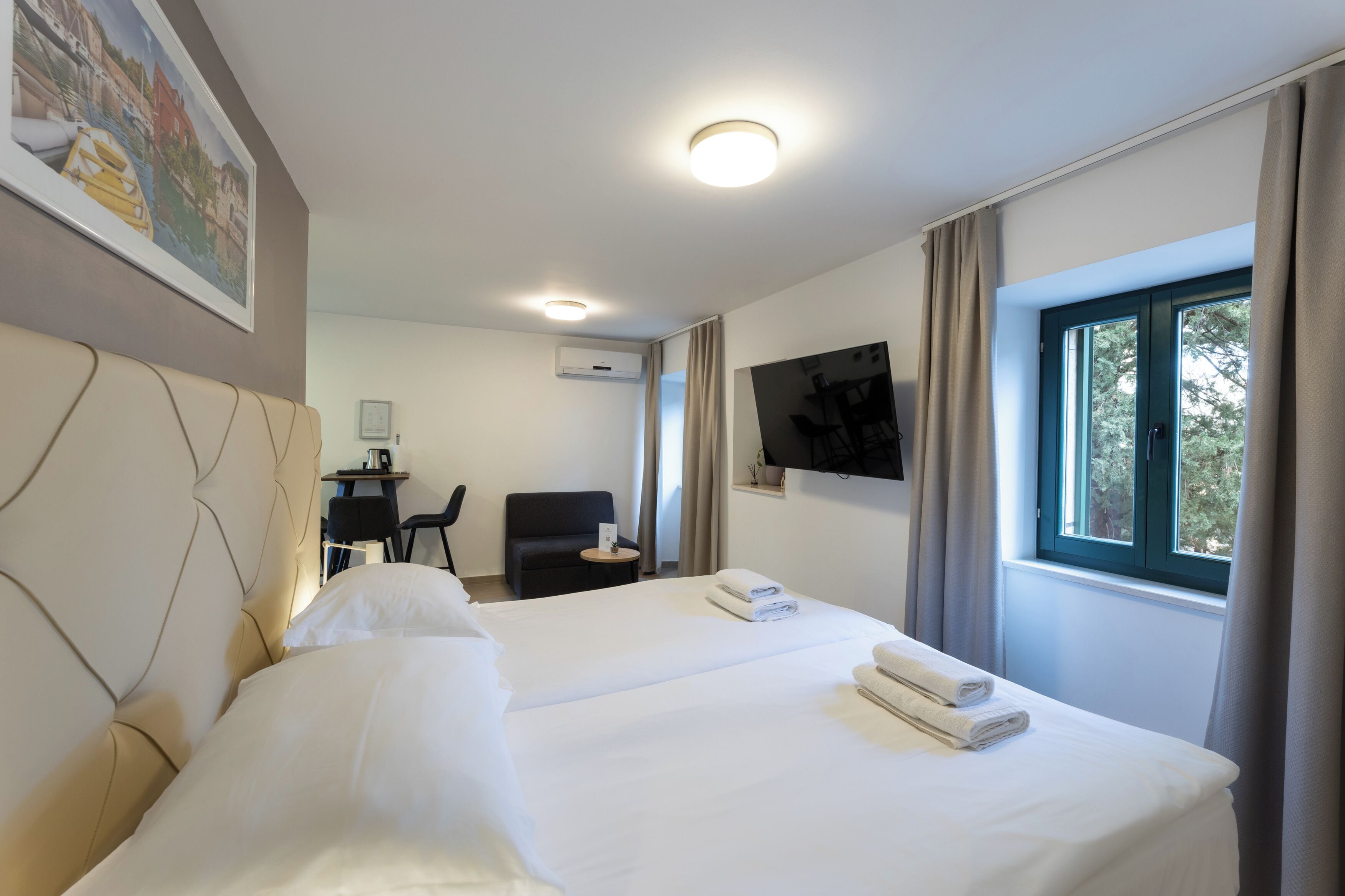 Habitación de hotel con dos camas, un escritorio, una silla, un televisor y una ventana con cortinas.