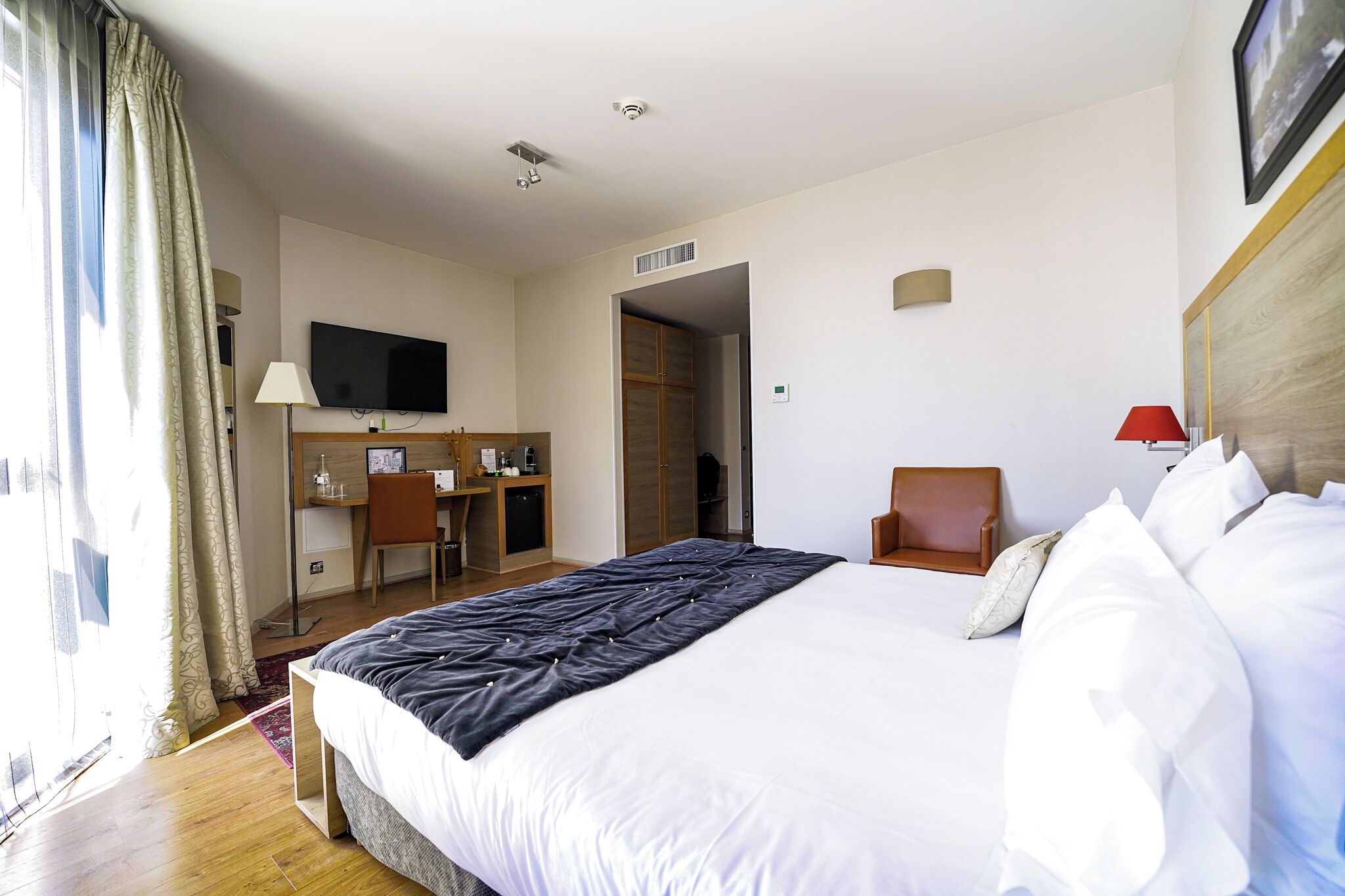 Habitación de hotel con una cama grande, un escritorio con silla, un televisor y una lámpara roja.