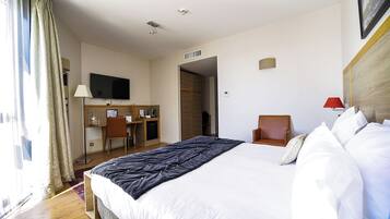 Habitación de hotel con una cama grande, un escritorio con silla, un televisor y una lámpara roja.