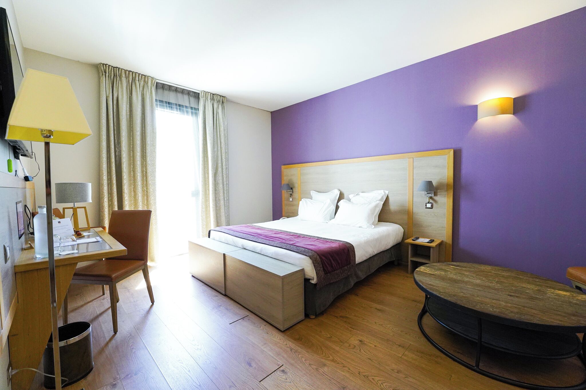 Una habitación de hotel con una cama, un escritorio, una silla, una mesita y un cubo de basura.