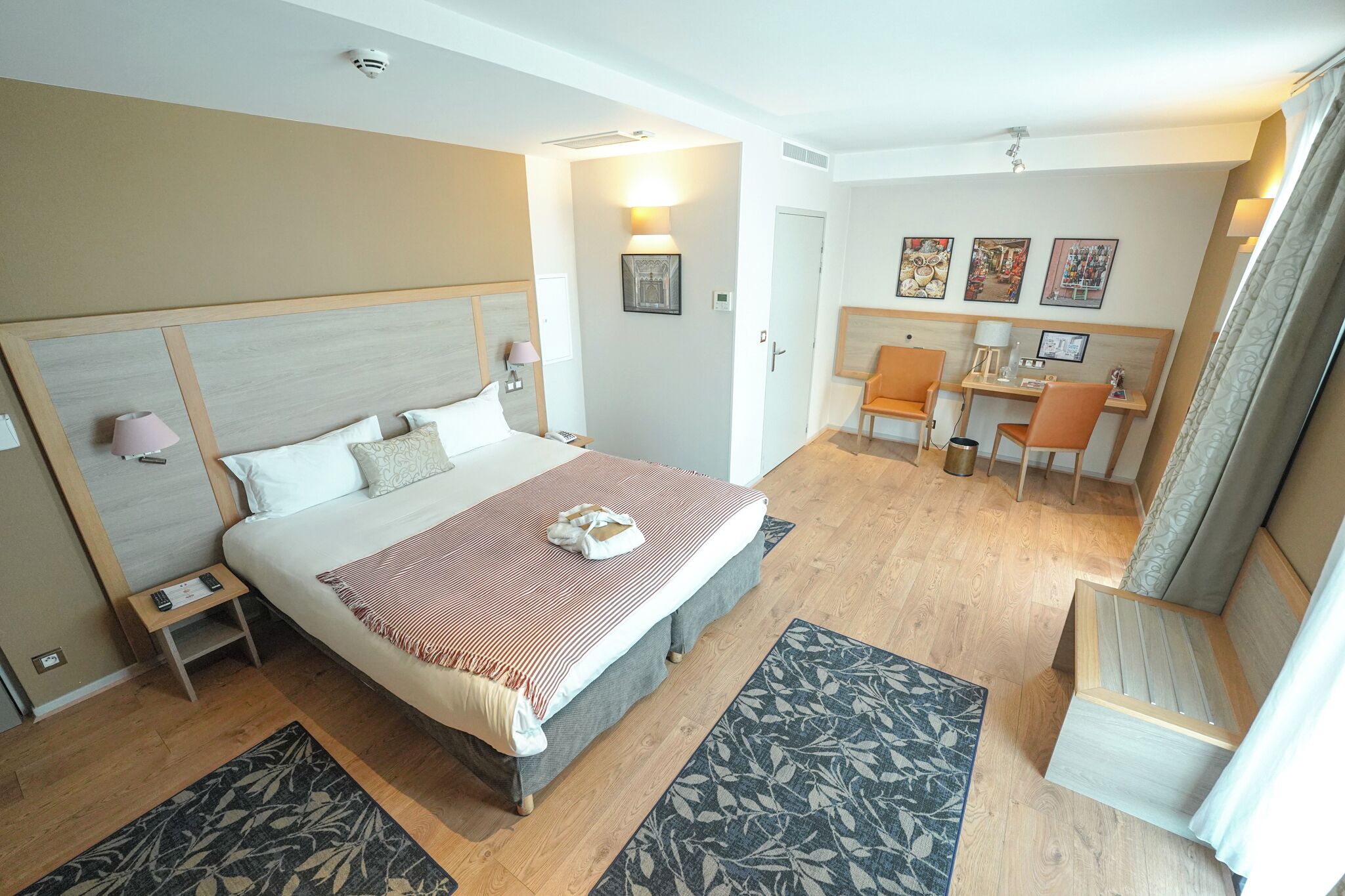 Une chambre d’hôtel avec un grand lit, des tables de chevet, un bureau avec des chaises et un petit coin salon.