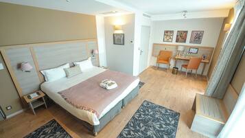 Une chambre d’hôtel avec un grand lit, des tables de chevet, un bureau avec des chaises et un petit coin salon.