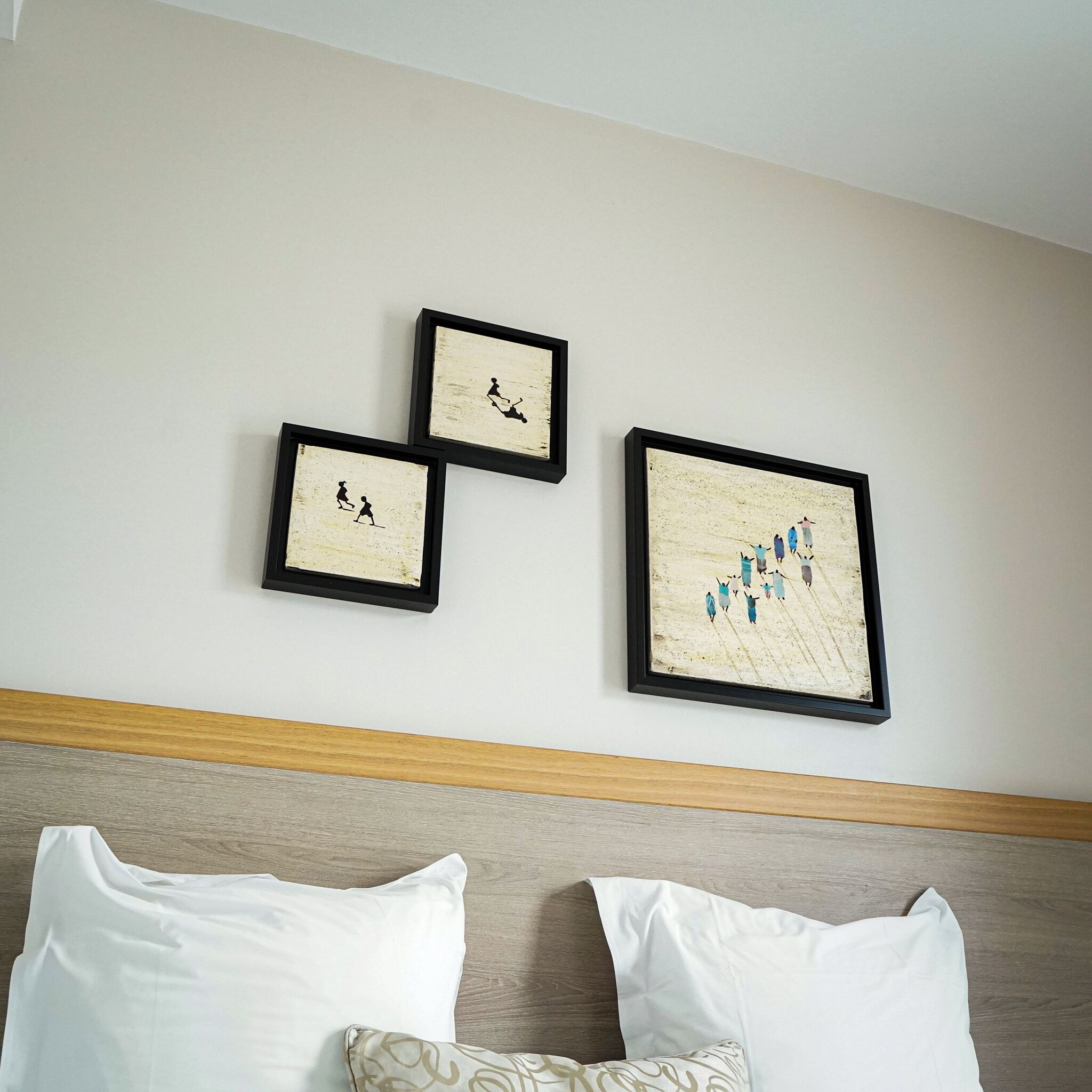 Een hotelkamer met een bed, twee kussens en drie kunstwerken in lijsten aan de muur.