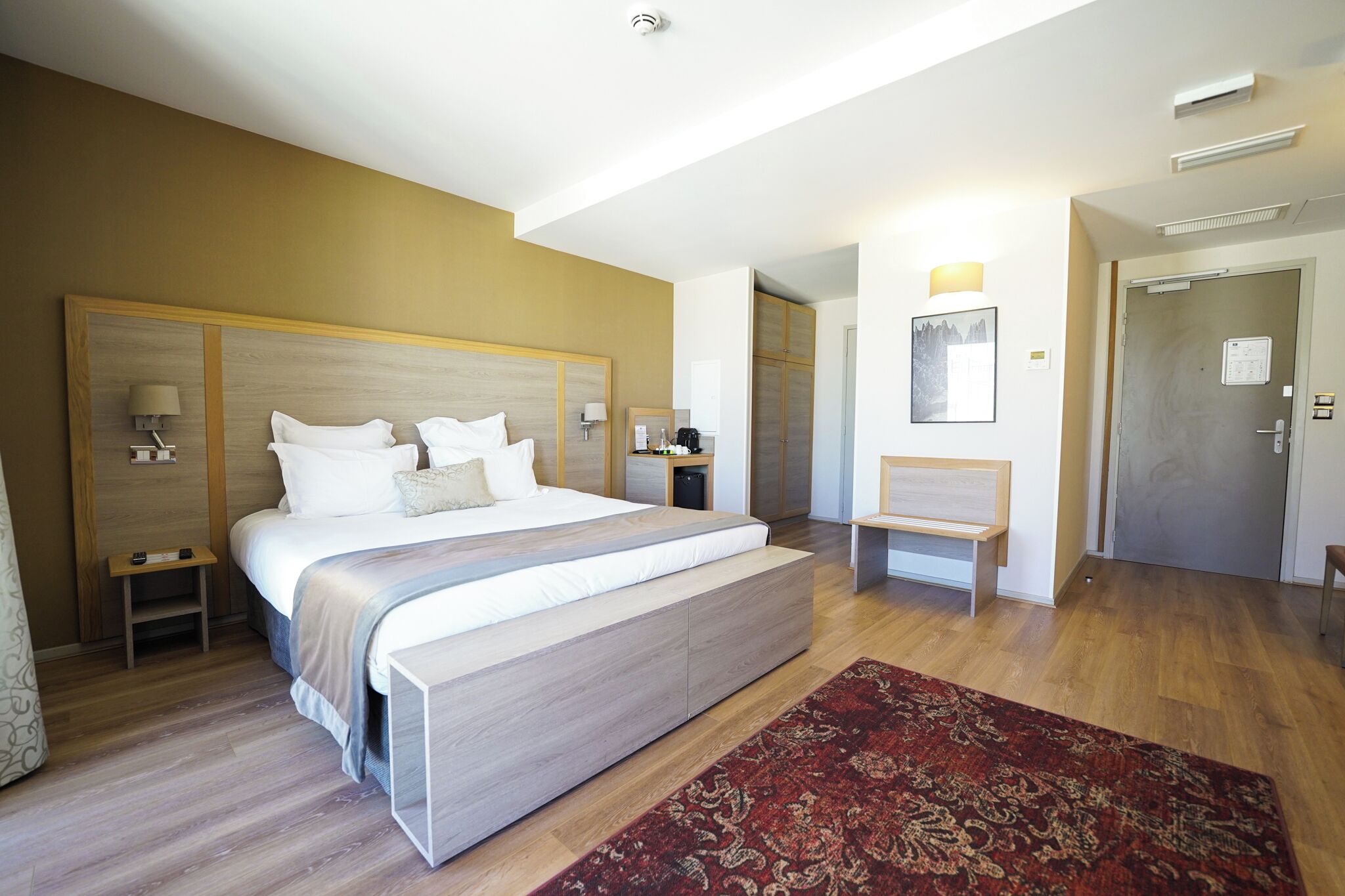 A modern hotel room with a large bed, bedside tables, a desk, and a chair.