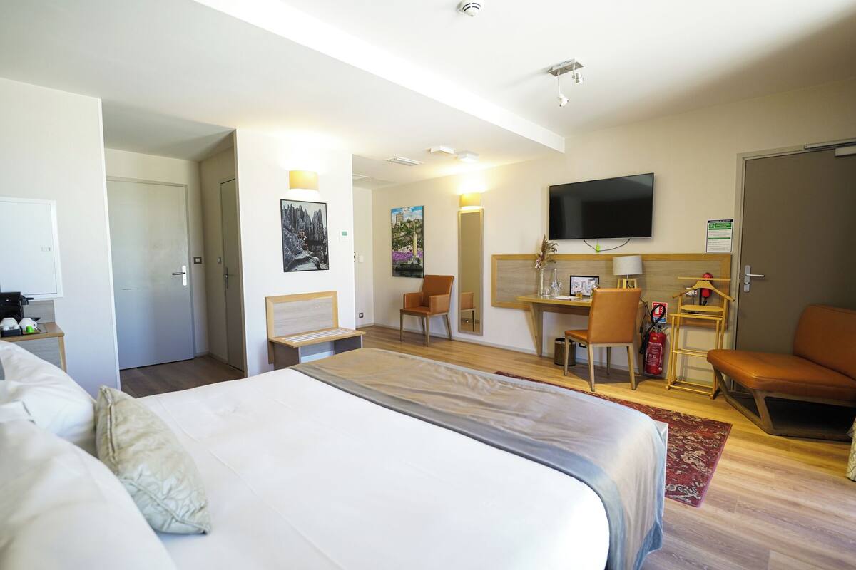 Una camera d'albergo con un letto grande, una scrivania, una sedia, una televisione e un estintore.