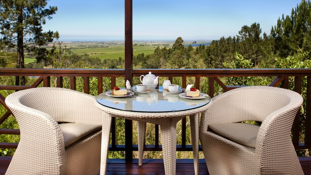 A wicker table with chairs on a balcony overlooking a scenic landscape. - ArendsRus Country Lodge (George)