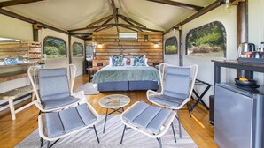 A cozy tented accommodation with a central bed, two wicker chairs, a small table, and a kitchenette. - ArendsRus Country Lodge (George)
