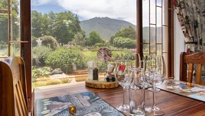 A dining table with wine glasses and a view of a mountainous landscape through large windows. - ArendsRus Country Lodge (George)