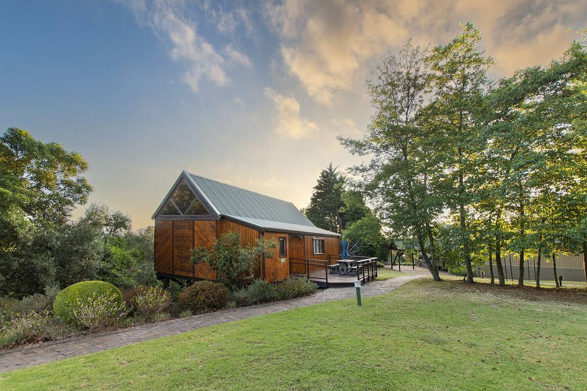 A wooden cabin with a sloped roof, surrounded by a well-maintained garden and trees.