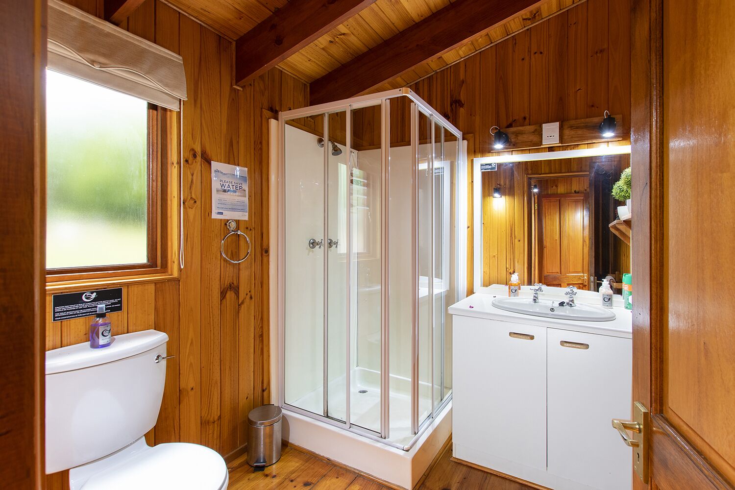 A wooden cabin bathroom with a toilet, shower, and sink.