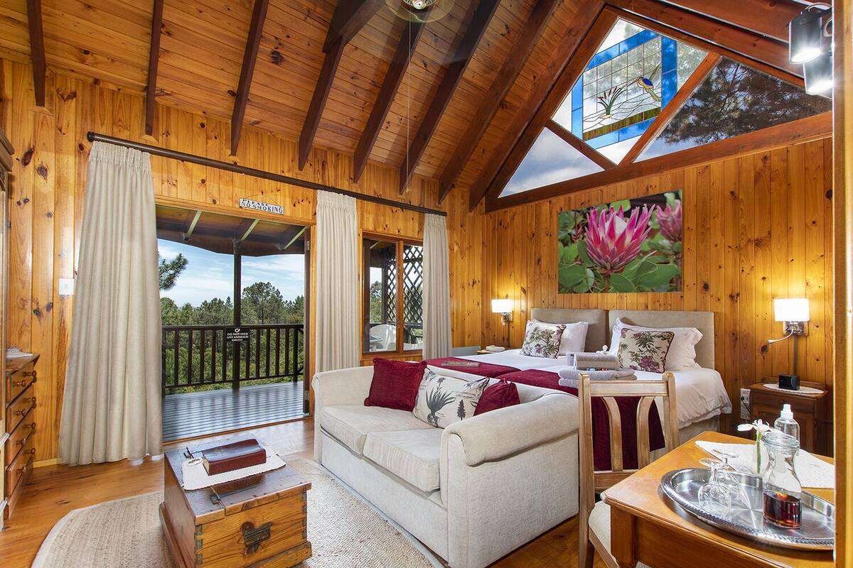 A wooden cabin interior with a bed, sofa, and dining area.