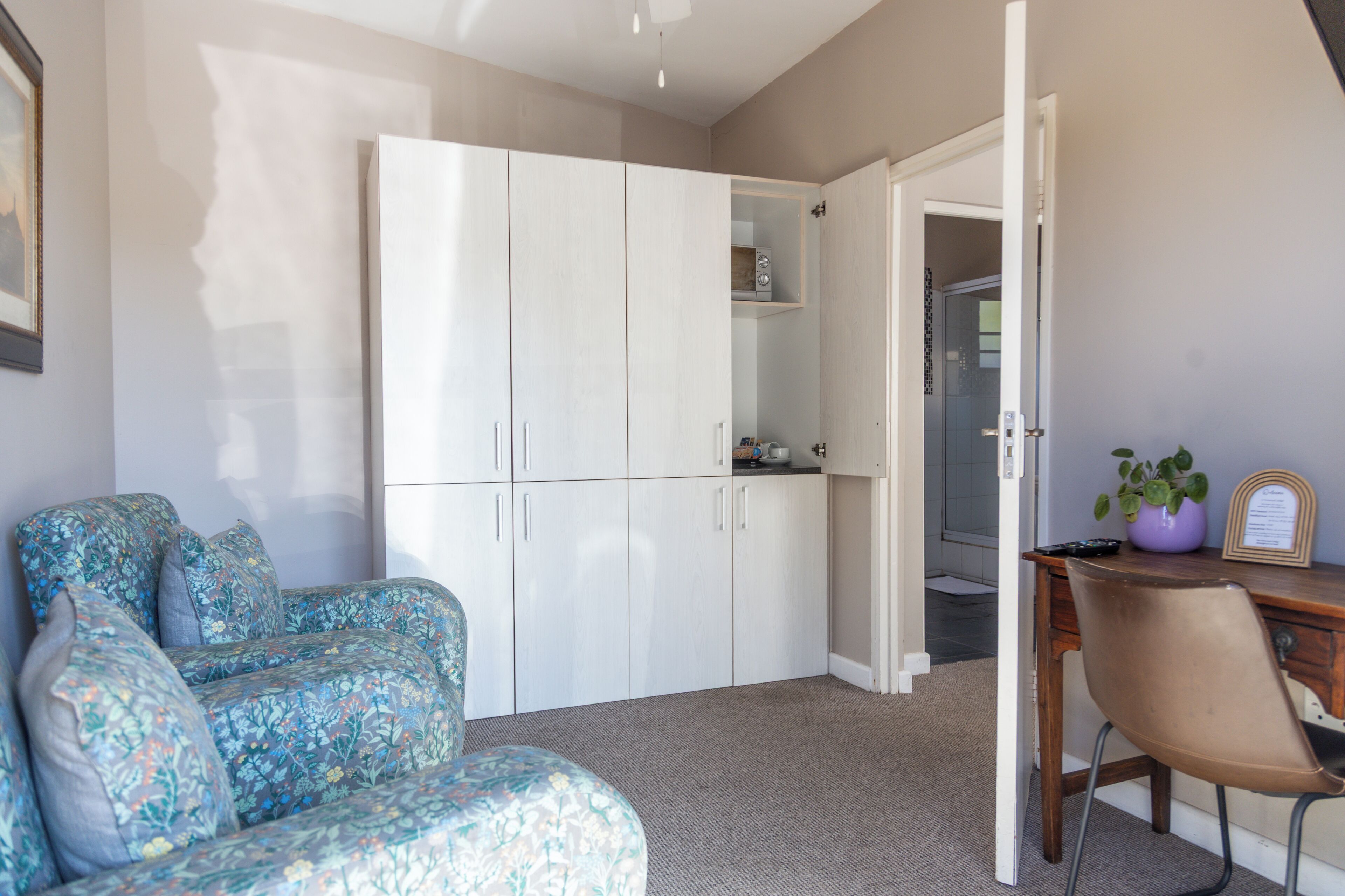A room with a large white wardrobe, a desk with a chair, and a floral-patterned sofa.