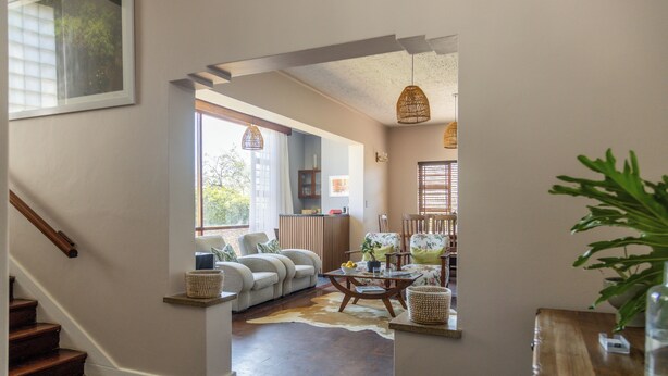 A living room with a sofa, a coffee table, and a dining table. There is a staircase leading to another level.
