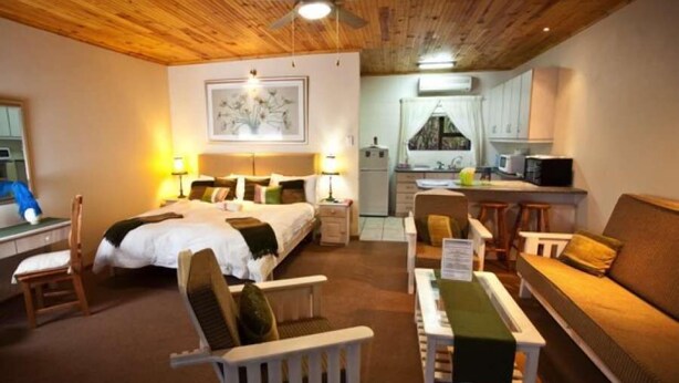 A cozy room with a bed, a desk, a chair, a sofa, and a kitchenette. - Cul de Sac (Oudtshoorn)