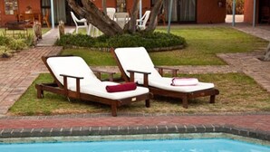 Two wooden lounge chairs with white cushions and red pillows by a pool. - Cul de Sac (Oudtshoorn)