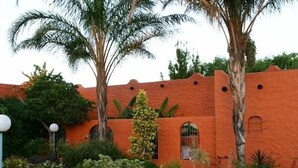 A building with a terracotta facade, arched windows, and a palm tree in the foreground. - Cul de Sac (Oudtshoorn)