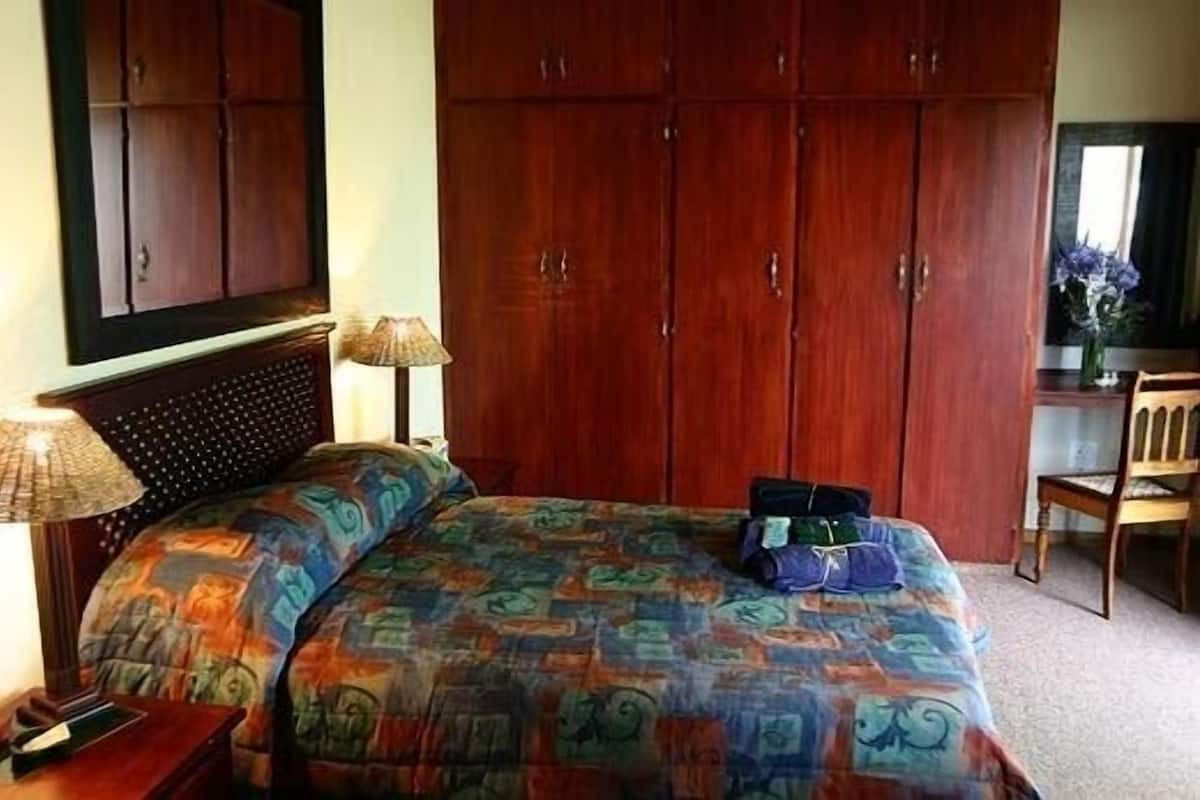 A bedroom with a large bed, a wardrobe, a desk with a lamp, and a chair.