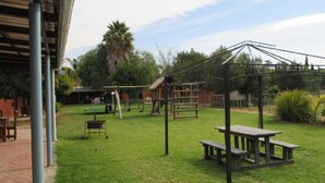 A grassy outdoor area with picnic tables, a swing set, and a covered structure. - Cul de Sac (Oudtshoorn)
