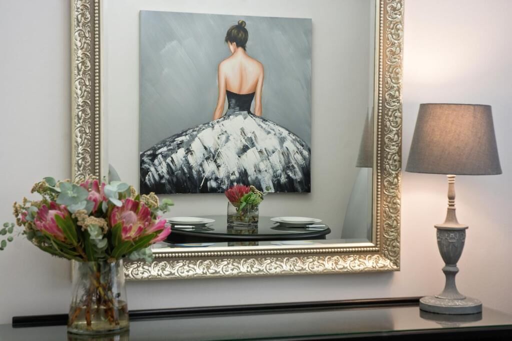 A framed painting of a woman in a dress, a vase with flowers, and a table lamp.