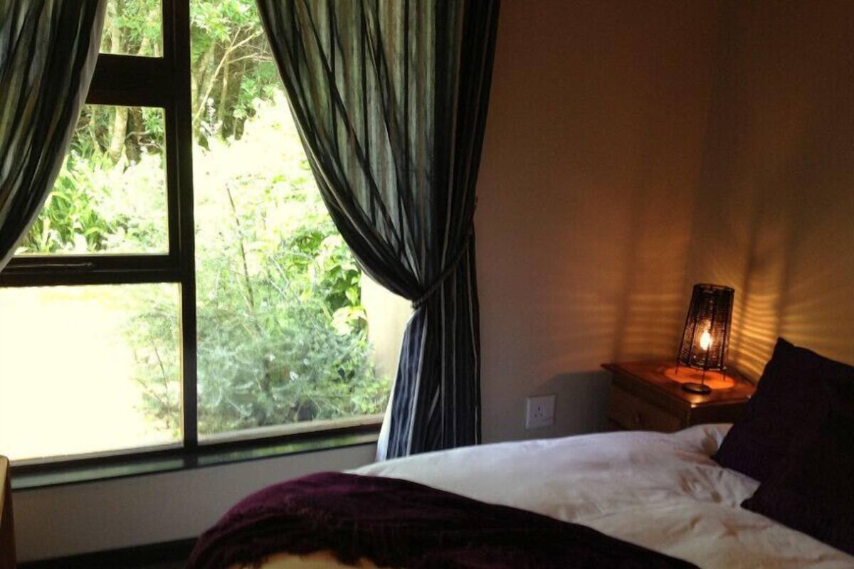 A bedroom with a bed, a nightstand with a lamp, and a window with curtains.