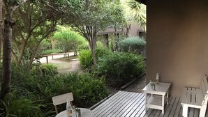 An outdoor wooden deck with a table and chairs, surrounded by lush greenery and a pathway. - Clairewood (Wilderness)