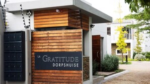 A modern building entrance with a wooden panel and a sign reading "LA GRATITUDE DORPSHUISE".