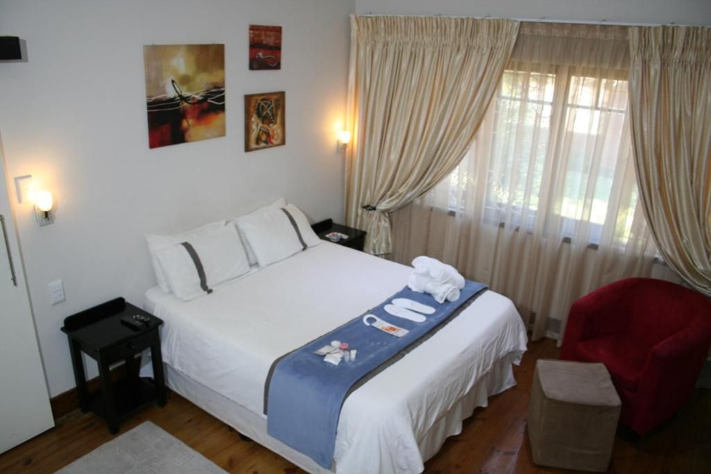 Una habitación de hotel con cama, mesita de noche, una silla roja y ventana con cortinas.