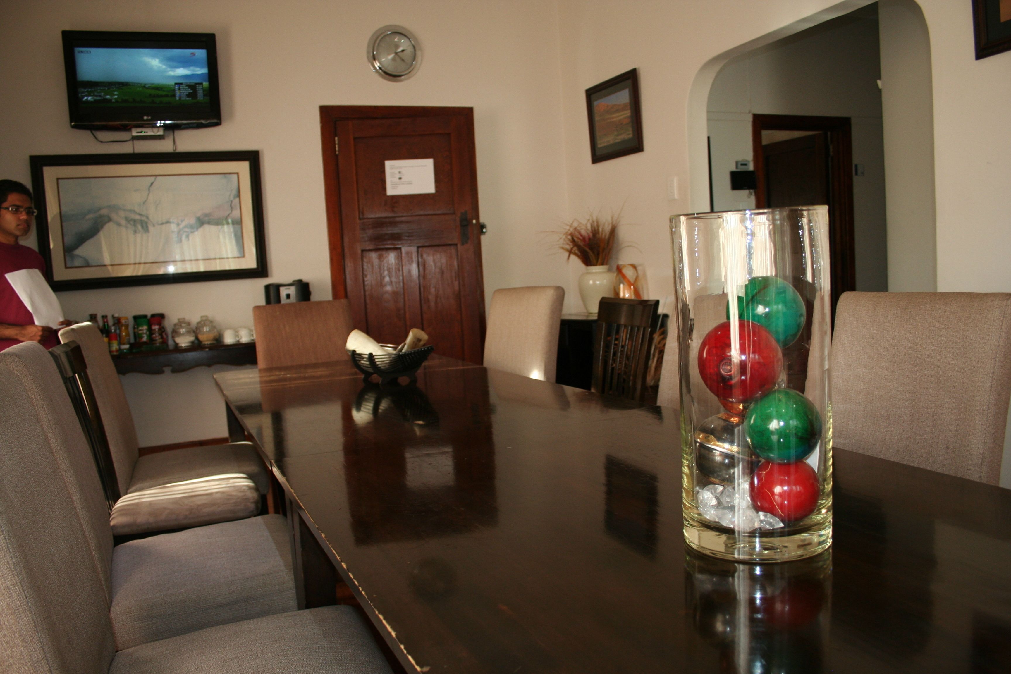 A conference room with a wooden table, chairs, a television, and a decorative glass vase with colorful balls.