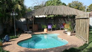 A backyard with a swimming pool, a wooden pergola, and outdoor seating. - Thembelihle Guest House (Pietermaritzburg)