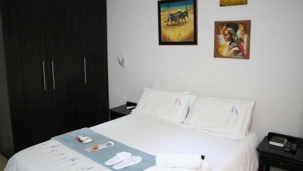 A hotel room with a large wardrobe, a bed with white linens, and two paintings on the wall. - Thembelihle Guest House (Pietermaritzburg)