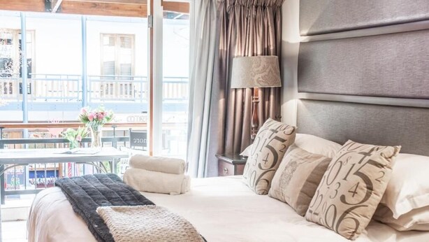 A hotel room with a large bed, a view of the city, and a balcony with a table and chairs.