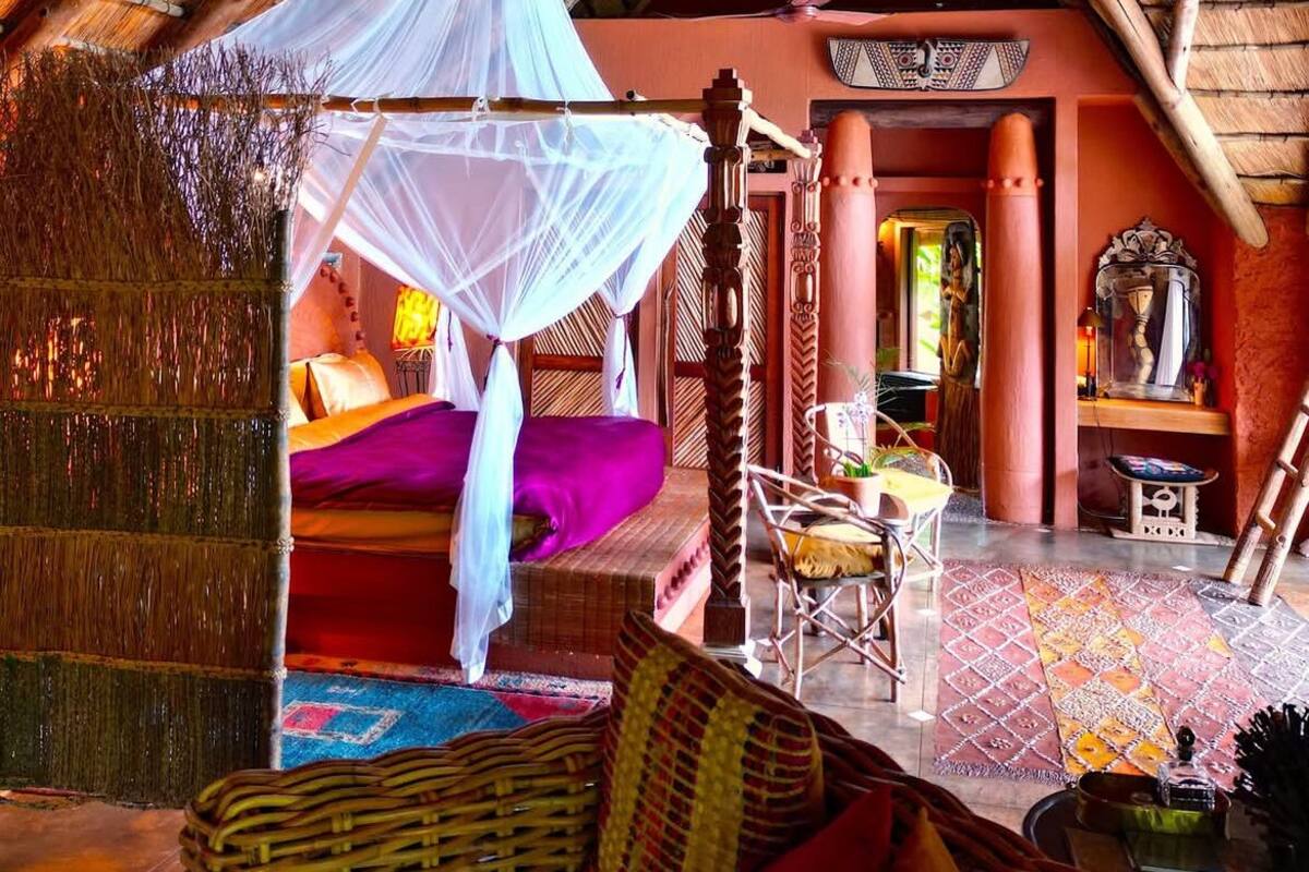 A room with a thatched roof, a bed with a canopy, a wicker sofa, and a decorative mirror.