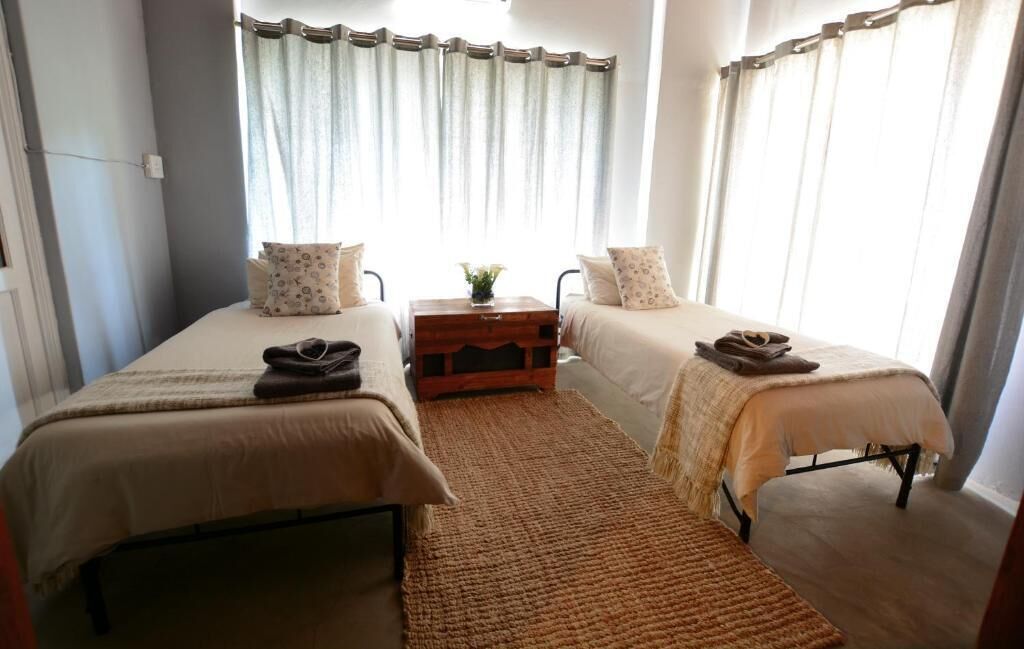 Un dormitorio con dos camas individuales, una mesita de noche de madera y un ventanal con cortinas.