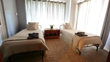 Un dormitorio con dos camas individuales, una mesita de noche de madera y un ventanal con cortinas.