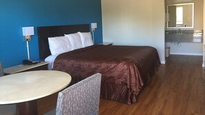 A hotel room with a bed, bedside table, chair, and a small round table. - Super Stay Inn (North Little Rock)