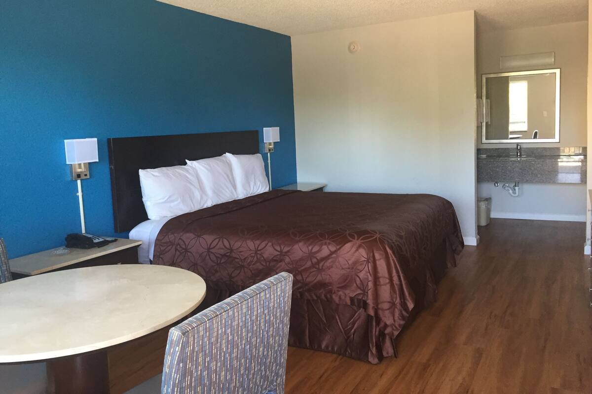 A hotel room with a bed, bedside table, chair, and a small round table.