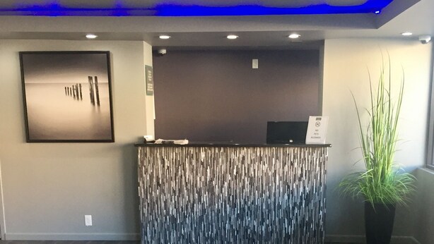 A reception area with a modern design, featuring a textured wall, a reception desk, and a potted plant. - Super Stay Inn (North Little Rock)