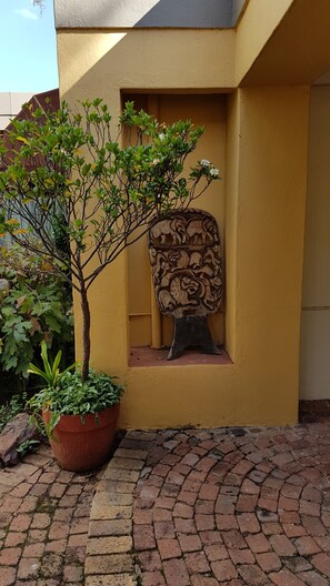 A potted plant, a carved wooden panel, and a brick pathway. - Jubilee Lodge Guest House (Randburg)