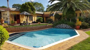 A swimming pool with a tiled edge, surrounded by a brick patio and lush greenery. - Jubilee Lodge Guest House (Randburg)