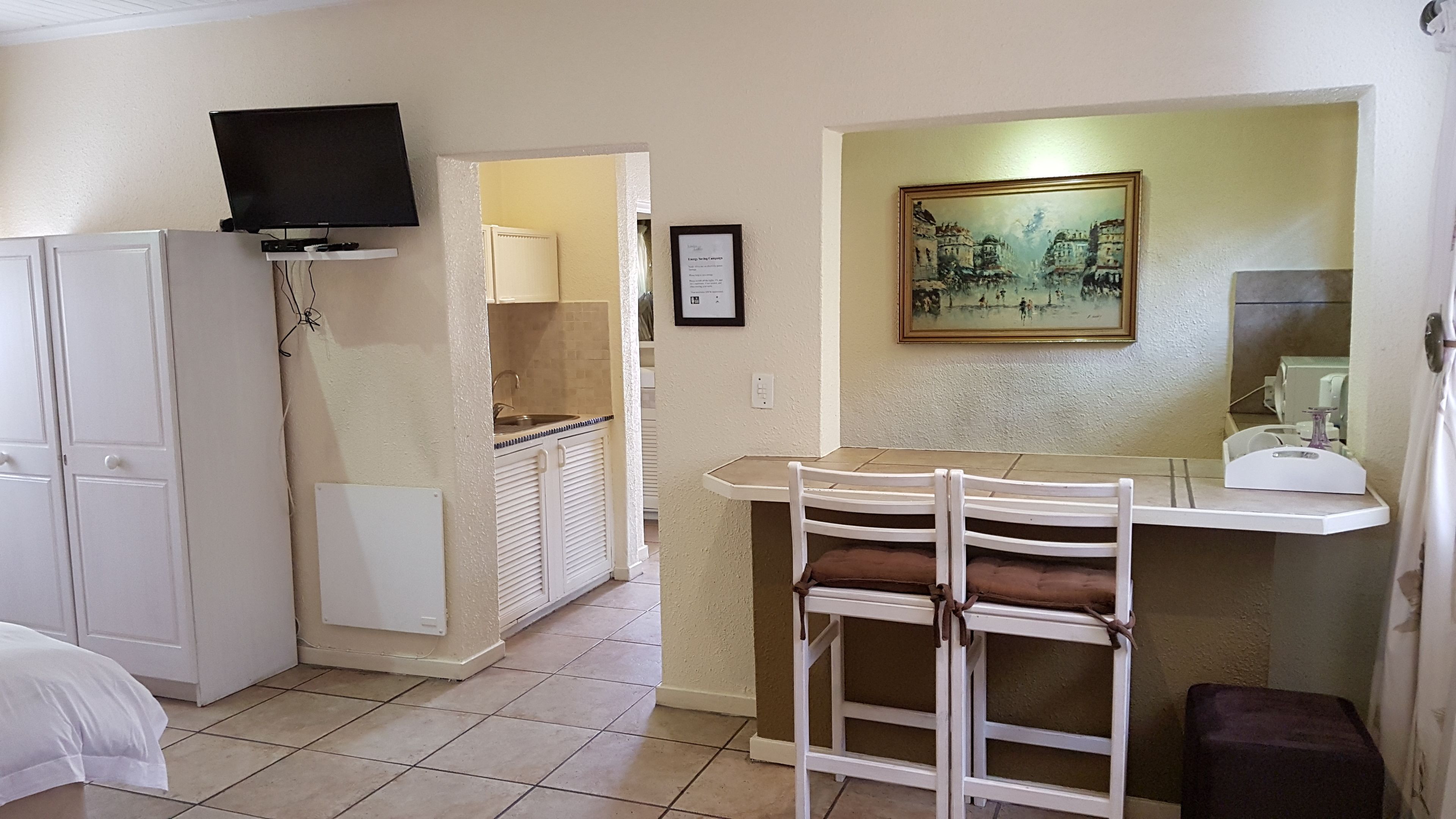 A compact kitchen with a dining area, a TV mounted above the counter, and a painting on the wall.