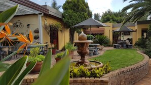 A courtyard with a fountain, potted plants, outdoor seating, and a pergola.