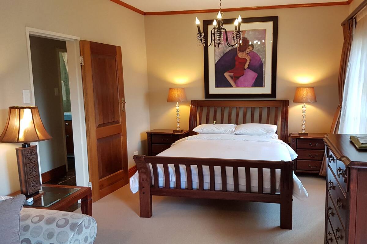 A hotel room with a wooden bed, two bedside tables with lamps, a television, a dresser, and a door leading to another room.